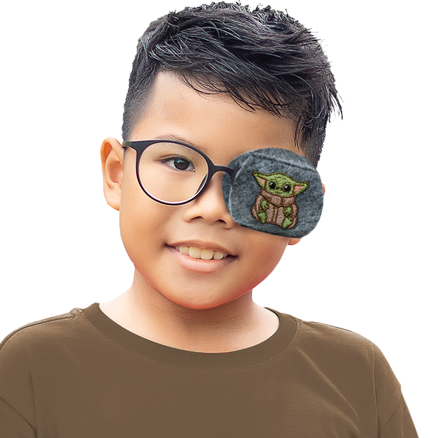 A young boy wearing a brown long-sleeve shirt and round black eyeglasses, with an eye patch over one eye featuring a green embroidered character on a gray background, set against a solid white studio backdrop.